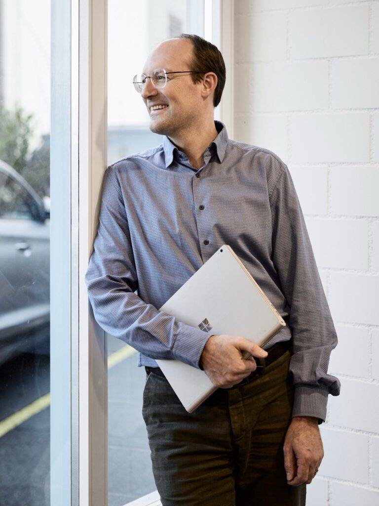 Lächelnder Mann mit Laptop am Fenster, Business-Porträt – Fotograf Winterthur, Fotostudio