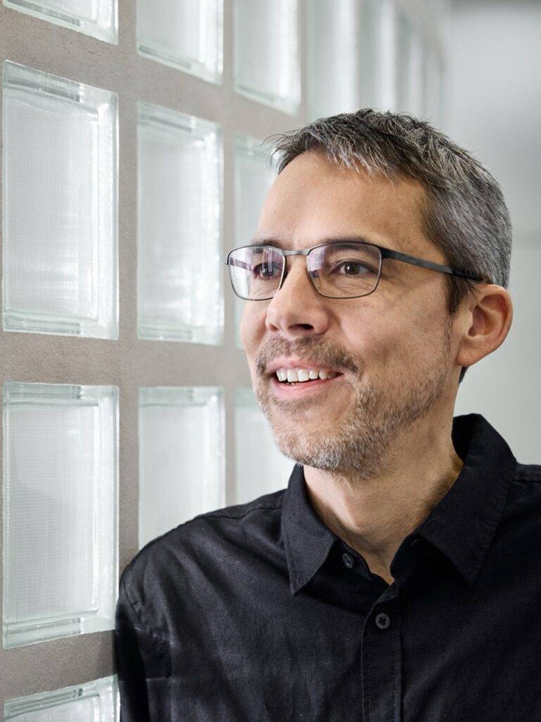 Lächelnder Mann mit Brille vor Glasbausteinwand, Porträt – Fotograf Winterthur, Fotostudio