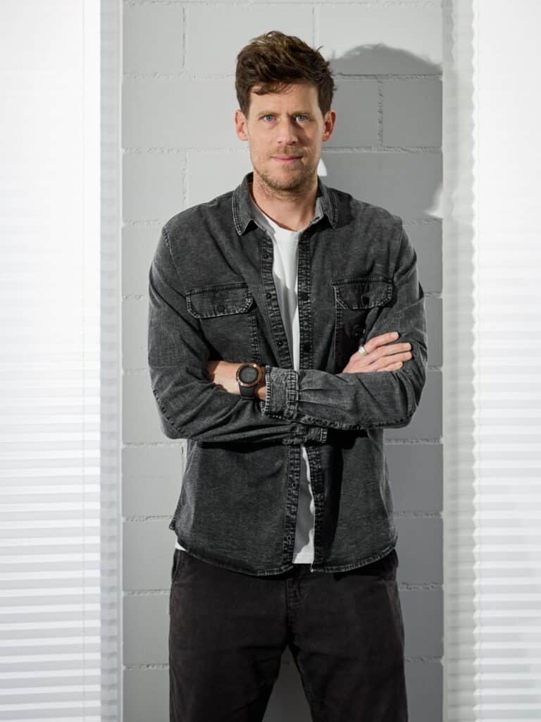 Mann mit verschränkten Armen vor grauer Ziegelwand, lässig in Jeanshemd; Fotostudio, Fotograf Winterthur
