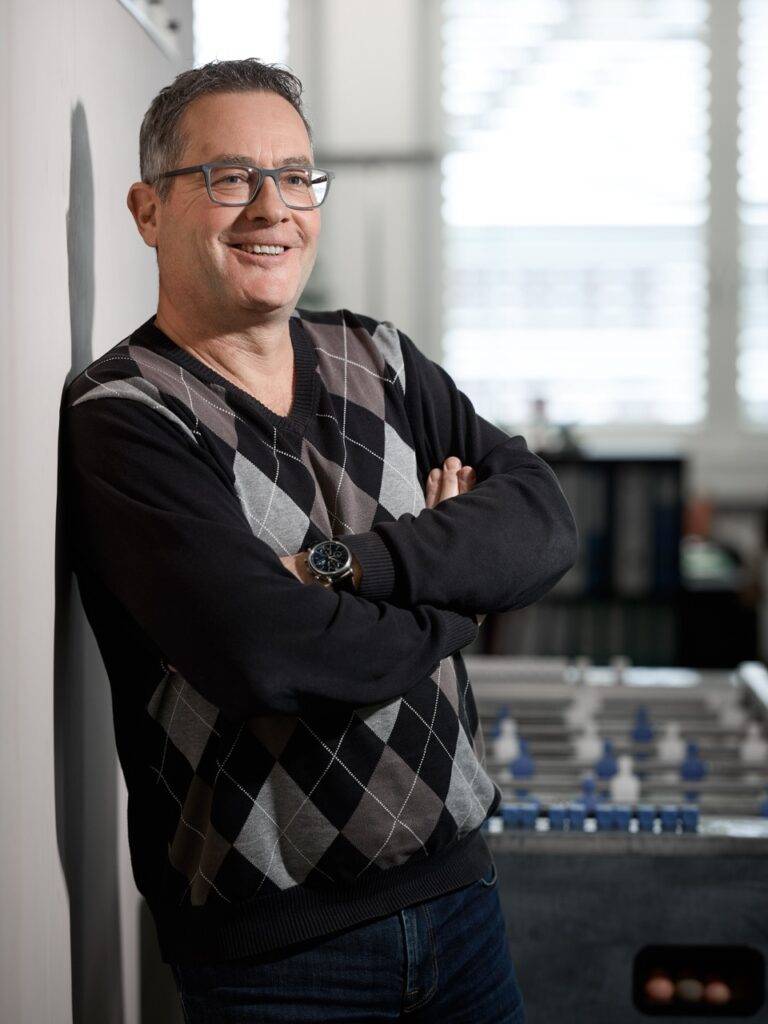 Lächelnder Mann mit Brille, verschränkte Arme vor Tischfussball im Büro – Fotostudio, Fotograf Winterthur