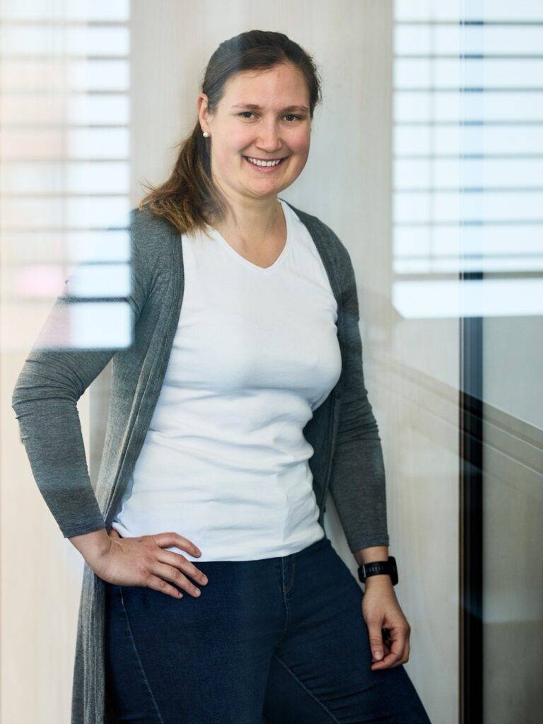 Lächelnde Frau in weißem Shirt und grauem Cardigan vor Glaswand, Business-Porträt – Fotograf Winterthur