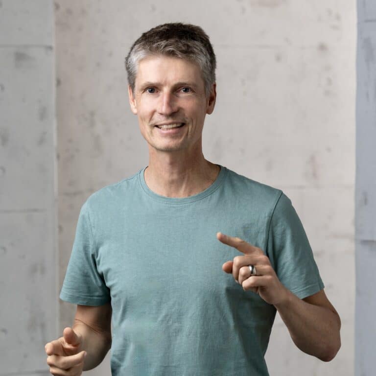 Lächelnder Andreas Gemperle, Inhaber VideoPhotoWorkers GmbH im türkis T‑Shirt, gestikulierend vor Betonwand, Fotostudio, Fotograf Winterthur